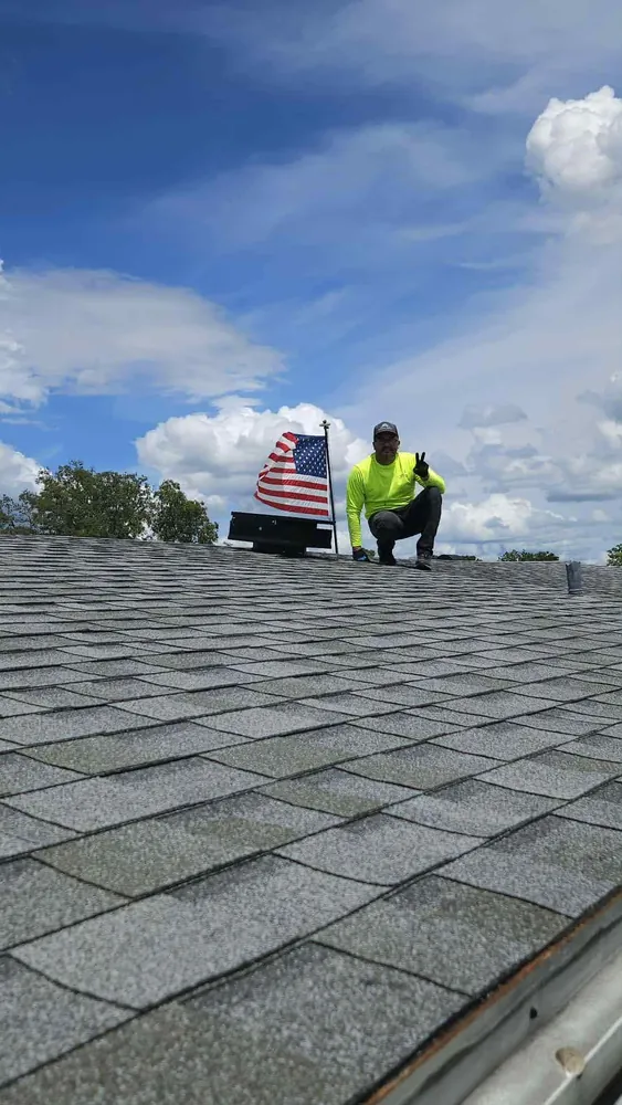 Arctic Attic installer on a Florida roof beside a newly installed solar attic fan and American flag