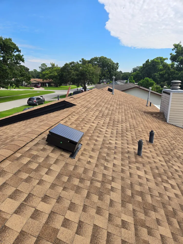 Solar attic fan mounted on a tan shingle roof near the ridge
