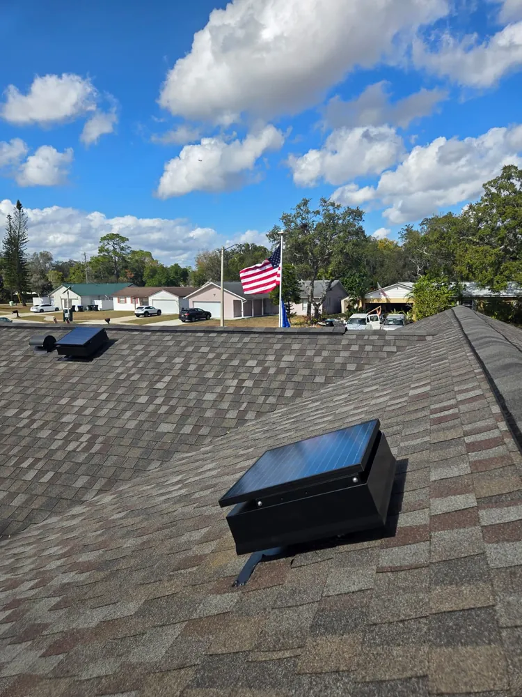 Solar attic fan on a shingle roof with an American flag flying across the street