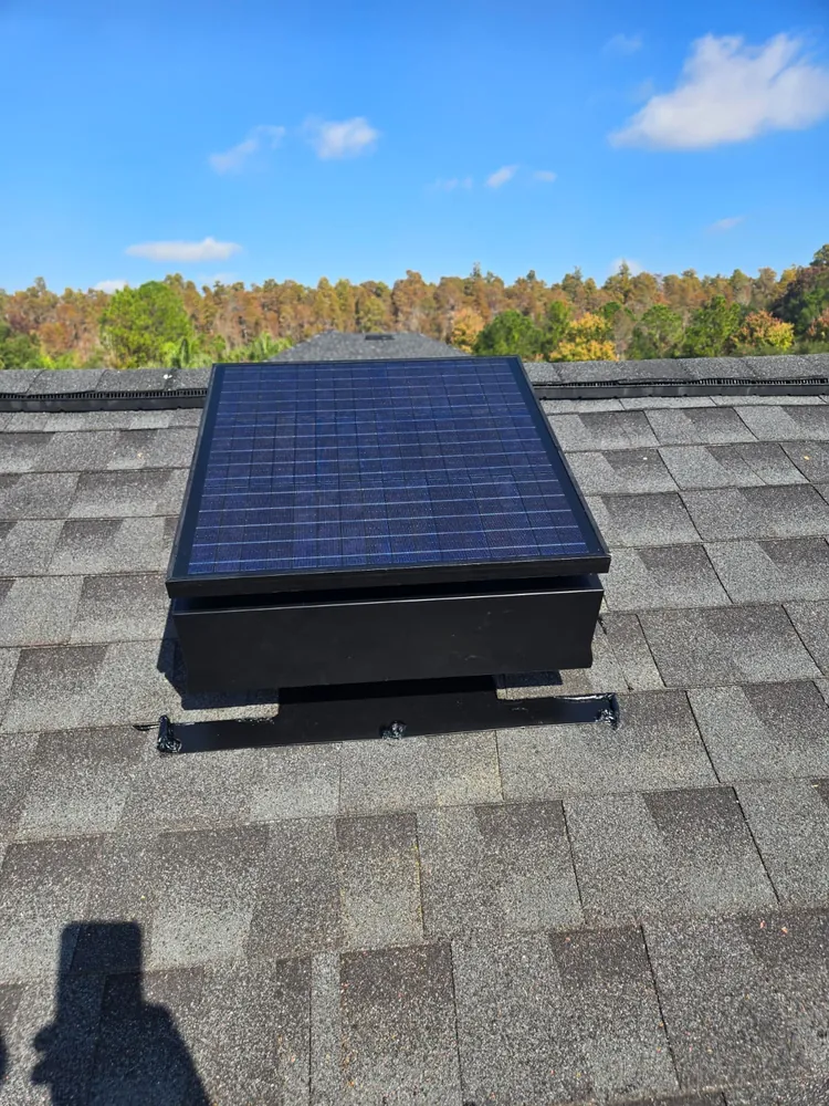 Solar attic fan mounted near the roof ridge under a clear blue sky